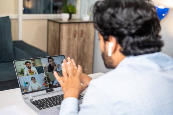 Young businessman making conference video call with colleagues on laptop at office - concept of online training, corporate meeting and project briefing.