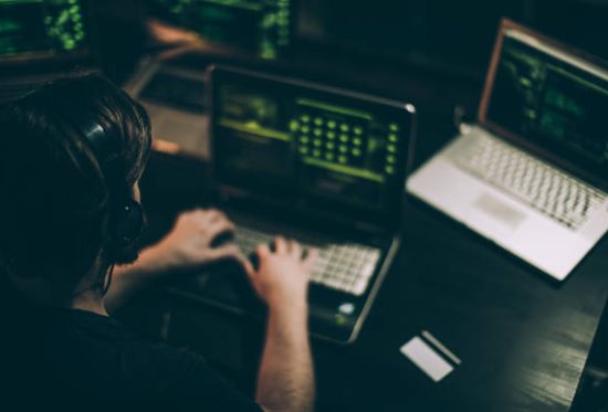 One man, sitting indoors surounded by computers, hacking crime is in motion, rear view.